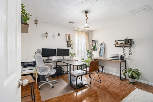 office area with baseboards, a textured ceiling, visible vents, and wood finished floors