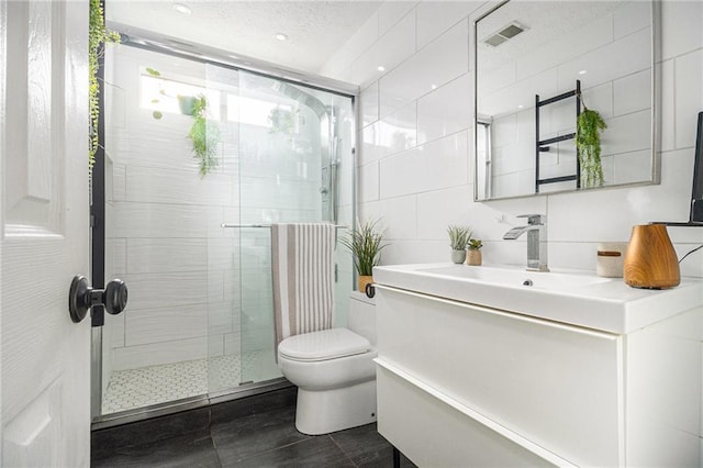 bathroom featuring toilet, vanity, visible vents, tile walls, and a shower stall