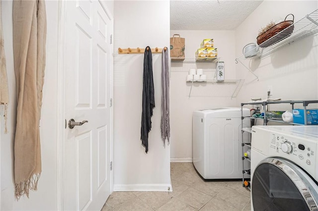 clothes washing area with a textured ceiling, light tile patterned flooring, laundry area, baseboards, and independent washer and dryer