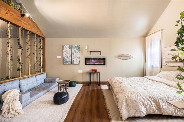 bedroom featuring lofted ceiling, a glass covered fireplace, wood finished floors, and baseboards