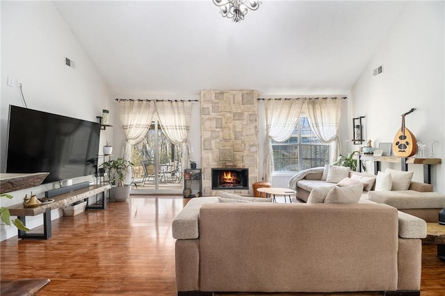 living area with a healthy amount of sunlight, high vaulted ceiling, wood finished floors, and a stone fireplace