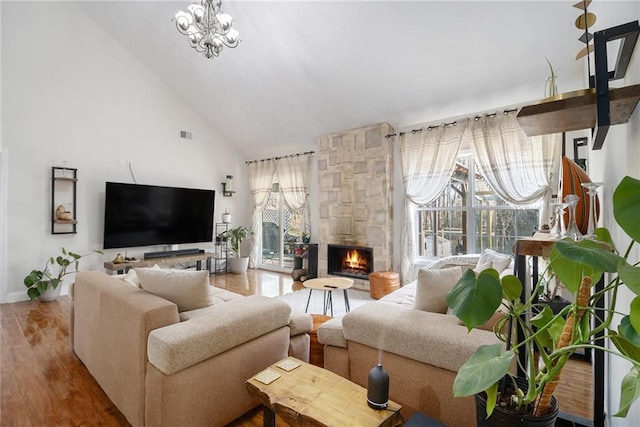 living area with high vaulted ceiling, a fireplace, an inviting chandelier, and wood finished floors