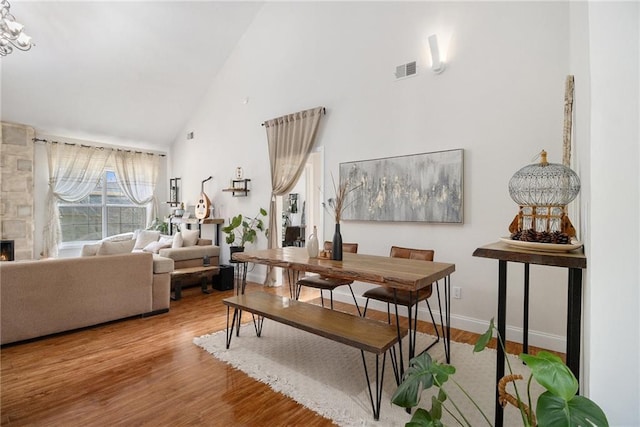 dining space featuring high vaulted ceiling, a stone fireplace, wood finished floors, visible vents, and baseboards