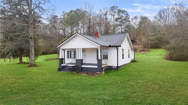 view of front of house featuring covered porch, roof with shingles, a front lawn, and a chimney