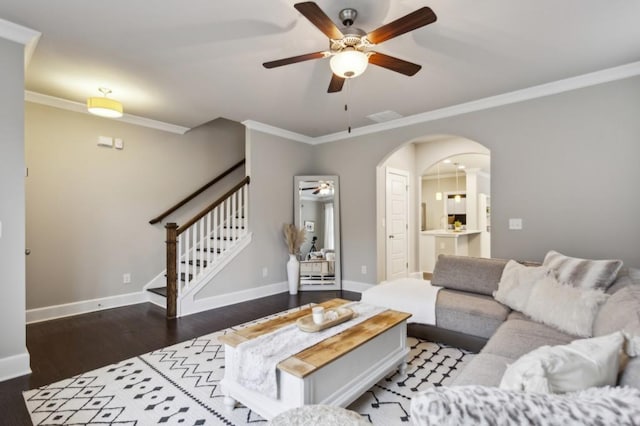 living area with a ceiling fan, crown molding, arched walkways, wood finished floors, and stairs