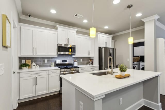kitchen featuring white cabinets, appliances with stainless steel finishes, a sink, separate washer and dryer, and a center island with sink
