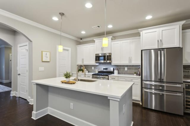 kitchen featuring white cabinets, appliances with stainless steel finishes, a sink, arched walkways, and tasteful backsplash