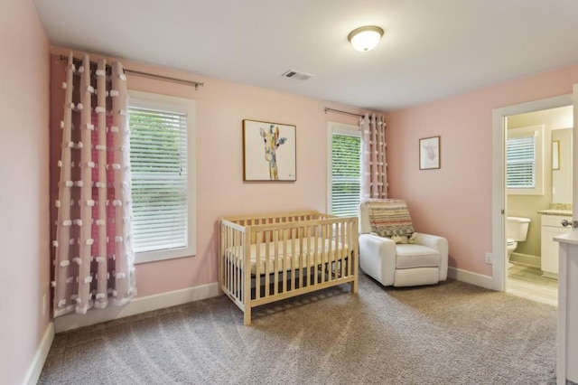 carpeted bedroom featuring baseboards, a crib, ensuite bath, and visible vents