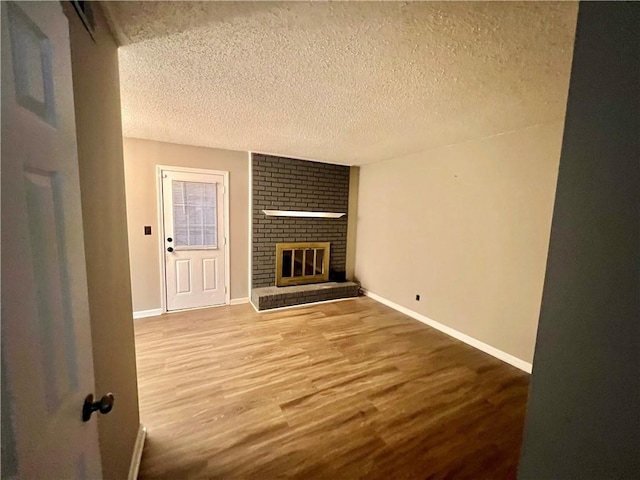 unfurnished living room with a textured ceiling, a brick fireplace, and hardwood / wood-style flooring