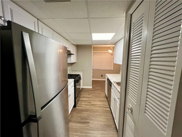 kitchen featuring a drop ceiling, white cabinets, stainless steel appliances, and light wood-type flooring