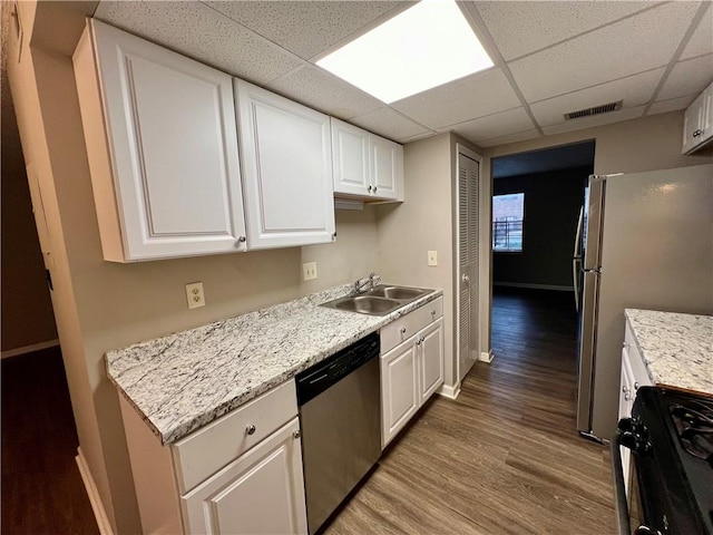 kitchen with stainless steel appliances, hardwood / wood-style floors, sink, a drop ceiling, and white cabinetry