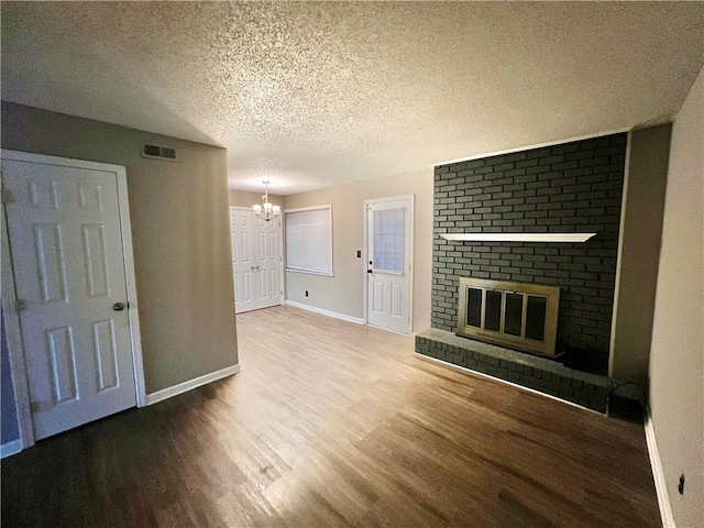 unfurnished living room with a notable chandelier, hardwood / wood-style flooring, a textured ceiling, and a brick fireplace