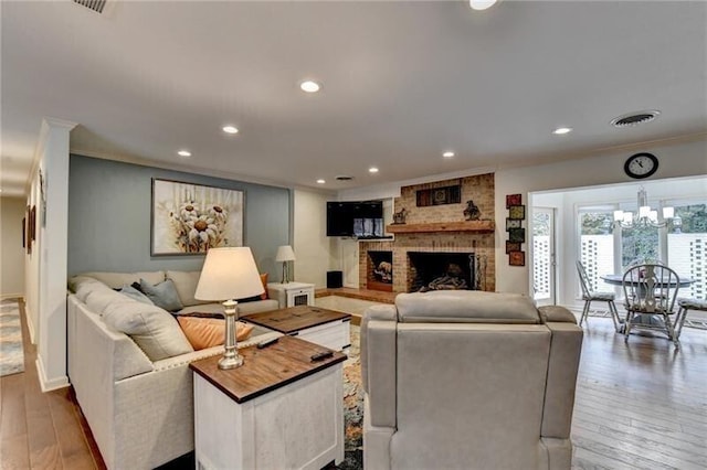 living room with visible vents, wood-type flooring, ornamental molding, a brick fireplace, and recessed lighting