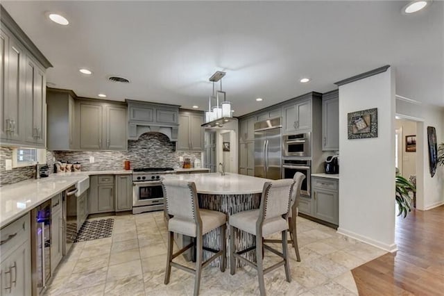 kitchen with decorative backsplash, gray cabinets, a kitchen bar, and high quality appliances