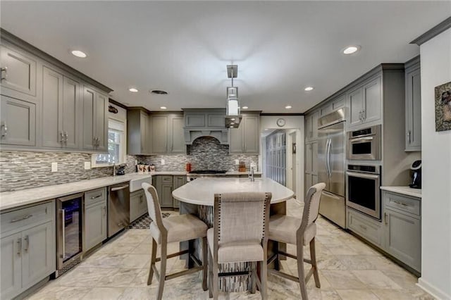 kitchen featuring wine cooler, tasteful backsplash, gray cabinets, appliances with stainless steel finishes, and a kitchen bar