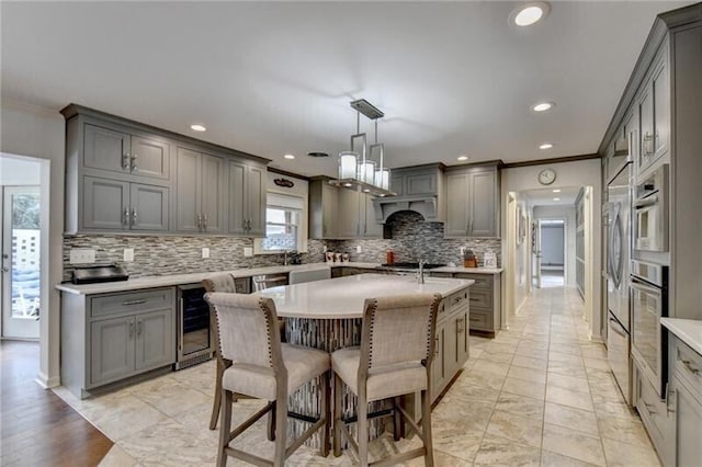 kitchen featuring appliances with stainless steel finishes, beverage cooler, an island with sink, and gray cabinetry