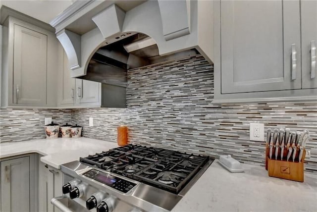 kitchen featuring cooktop, light countertops, backsplash, gray cabinetry, and premium range hood