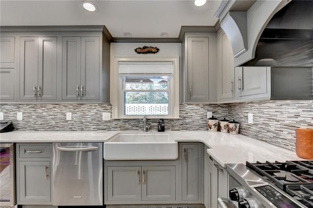 kitchen with appliances with stainless steel finishes, gray cabinets, a sink, and wall chimney range hood