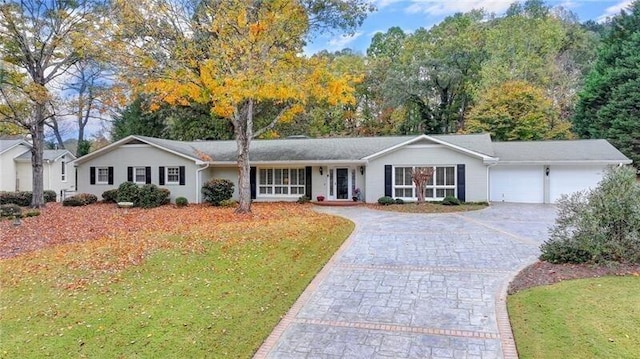 single story home featuring an attached garage, decorative driveway, and a front yard