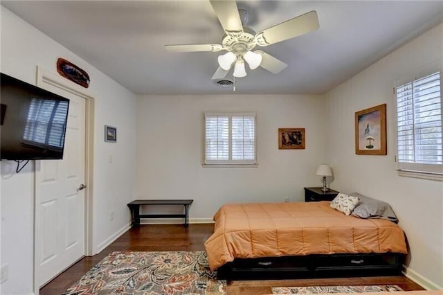 bedroom with a ceiling fan, visible vents, baseboards, and wood finished floors