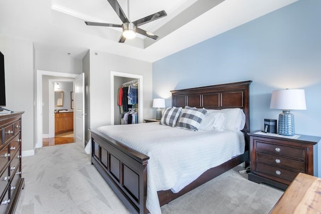 carpeted bedroom featuring ensuite bath, a walk in closet, a tray ceiling, a closet, and ceiling fan