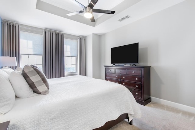 bedroom with light colored carpet, ceiling fan, and a tray ceiling