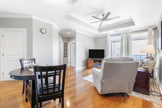 living room with crown molding, a raised ceiling, ceiling fan, and light wood-type flooring