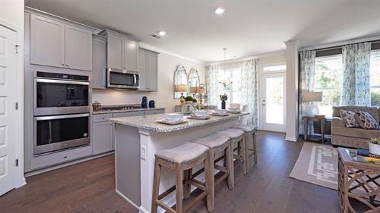 kitchen featuring appliances with stainless steel finishes, gray cabinets, dark hardwood / wood-style floors, a breakfast bar area, and an island with sink