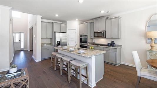 kitchen featuring appliances with stainless steel finishes, light stone counters, gray cabinetry, a kitchen island with sink, and a breakfast bar area