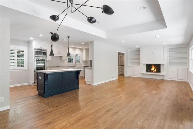 living room with built in features, light wood-type flooring, a brick fireplace, and a tray ceiling