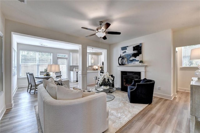 living room featuring ceiling fan, decorative columns, and light wood-type flooring