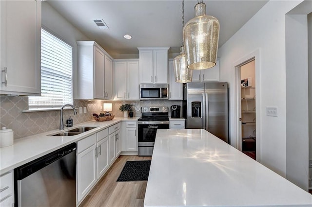 kitchen with white cabinetry, stainless steel appliances, sink, and pendant lighting