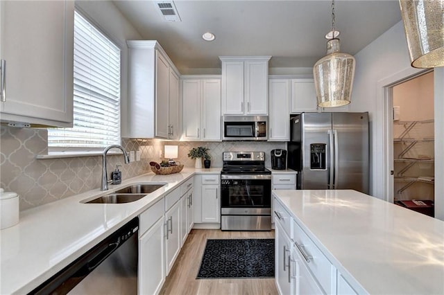 kitchen featuring white cabinets, hanging light fixtures, appliances with stainless steel finishes, light hardwood / wood-style floors, and sink