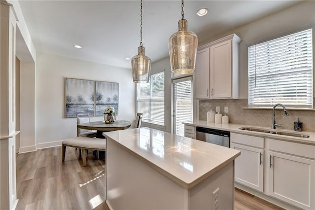 kitchen featuring sink, a kitchen island, decorative light fixtures, stainless steel dishwasher, and white cabinets