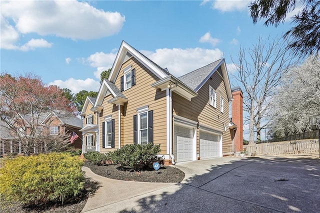 view of property exterior featuring fence, roof with shingles, a chimney, concrete driveway, and a garage