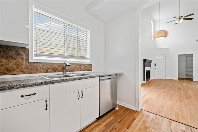 kitchen with a wealth of natural light, light wood-style flooring, a sink, stainless steel dishwasher, and white cabinetry