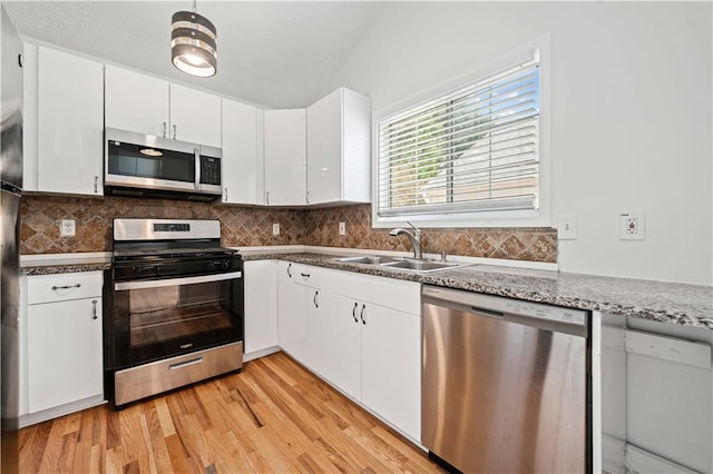 kitchen with light wood-style flooring, a sink, white cabinetry, stainless steel appliances, and decorative backsplash