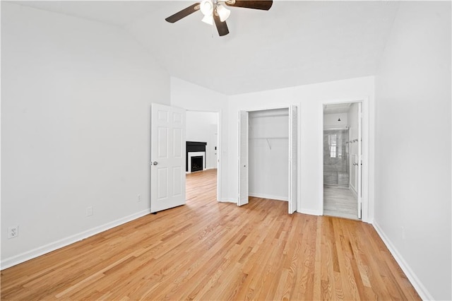 unfurnished bedroom featuring connected bathroom, baseboards, vaulted ceiling, light wood-style flooring, and a fireplace