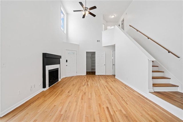 unfurnished living room featuring wood finished floors, stairway, baseboards, ceiling fan, and a tile fireplace