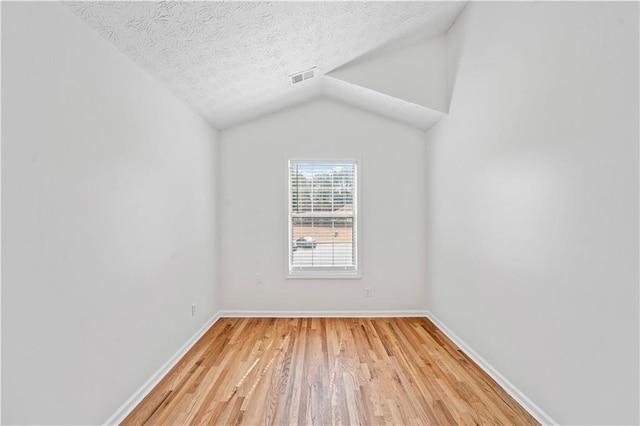 empty room featuring visible vents, baseboards, light wood-style flooring, vaulted ceiling, and a textured ceiling