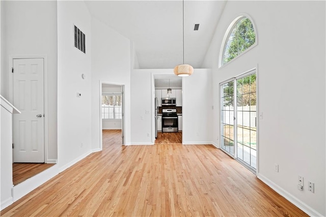 unfurnished dining area with light wood-style flooring, baseboards, visible vents, and high vaulted ceiling