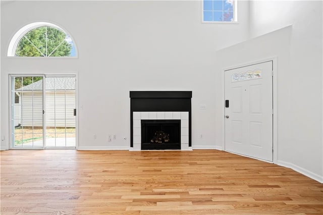 unfurnished living room featuring a high ceiling, baseboards, light wood-type flooring, and a tile fireplace