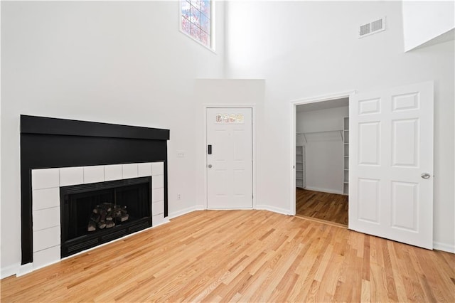 unfurnished living room with baseboards, wood finished floors, visible vents, and a tile fireplace