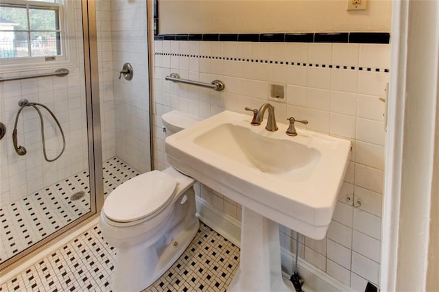 bathroom with tile patterned floors, toilet, a shower with door, and tile walls