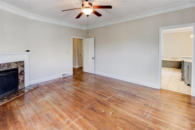 unfurnished living room featuring ornamental molding, light wood-type flooring, ceiling fan, and a fireplace