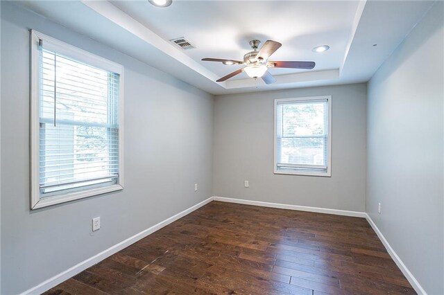 empty room with a tray ceiling, ceiling fan, and dark hardwood / wood-style floors