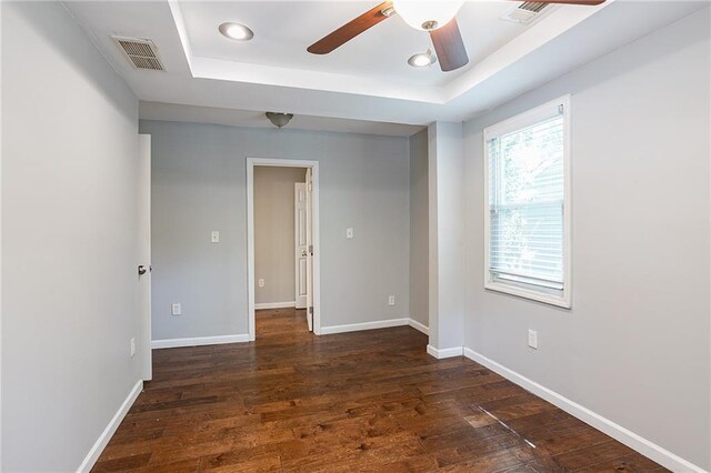 empty room featuring ceiling fan, a raised ceiling, and dark wood-type flooring