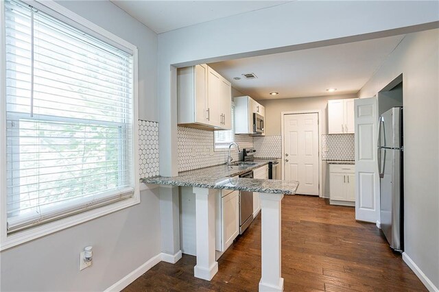 kitchen with light stone counters, appliances with stainless steel finishes, kitchen peninsula, and white cabinetry