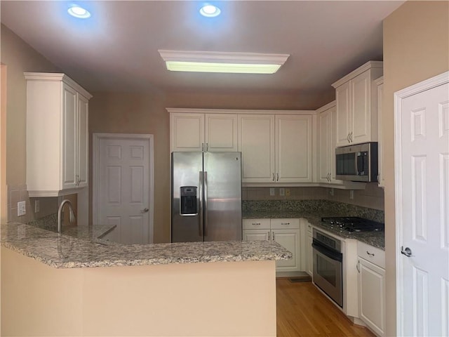 1919 Barrett Knoll Cir NW, Kennesaw, GA 30152 - kitchen with appliances with stainless steel finishes, a peninsula, light stone counters, light wood-style floors, and white cabinets