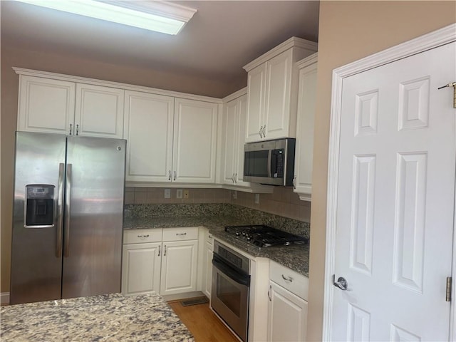 1919 Barrett Knoll Cir NW, Kennesaw, GA 30152 - kitchen with appliances with stainless steel finishes, white cabinetry, decorative backsplash, wood finished floors, and dark stone counters